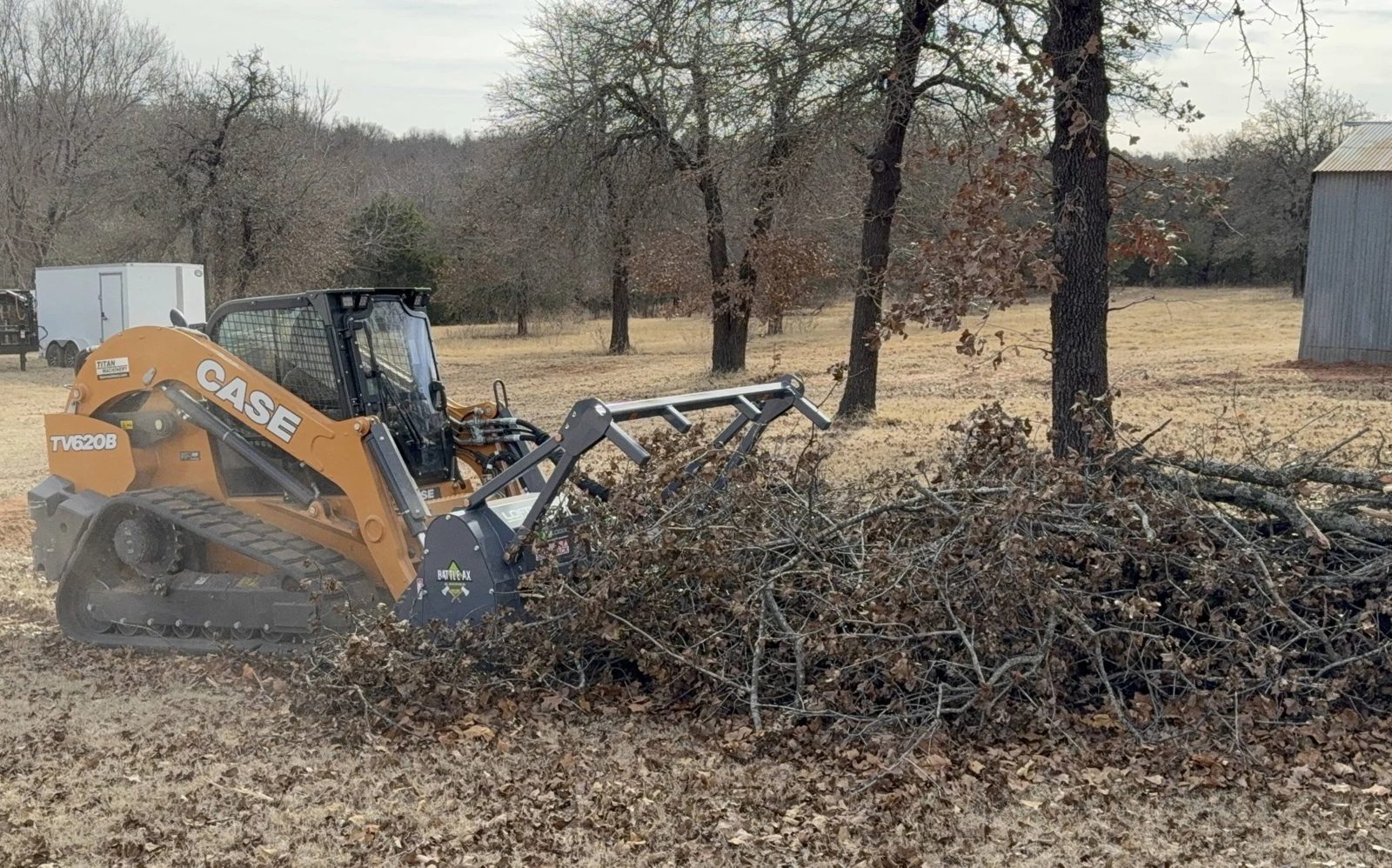 Track loader with a grapple bucket moving a brush pile